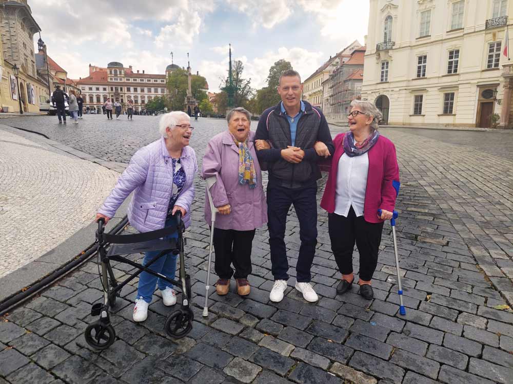 Foto von drei Seniorinnen und dem Reiseleiter der Silberweißfahrten, sie lachen ehr herzlich und stehen in Mitten einer schönen Altstadt.