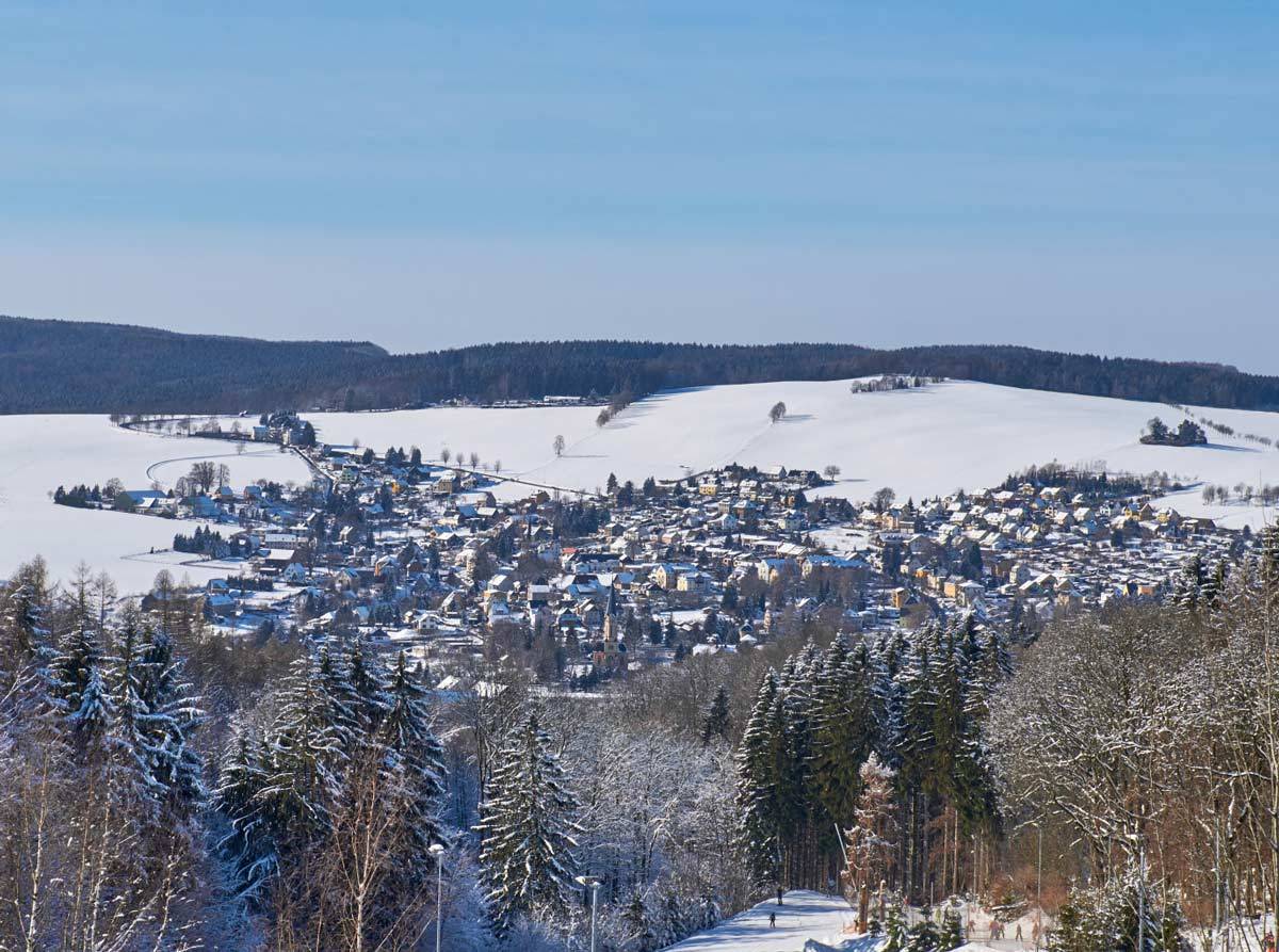 Atemberaubender Panoramaausblick auf weiße Berge, ei verschneites Dorf und grünen und von weißen Puderschnee bedeckten Bäumen.