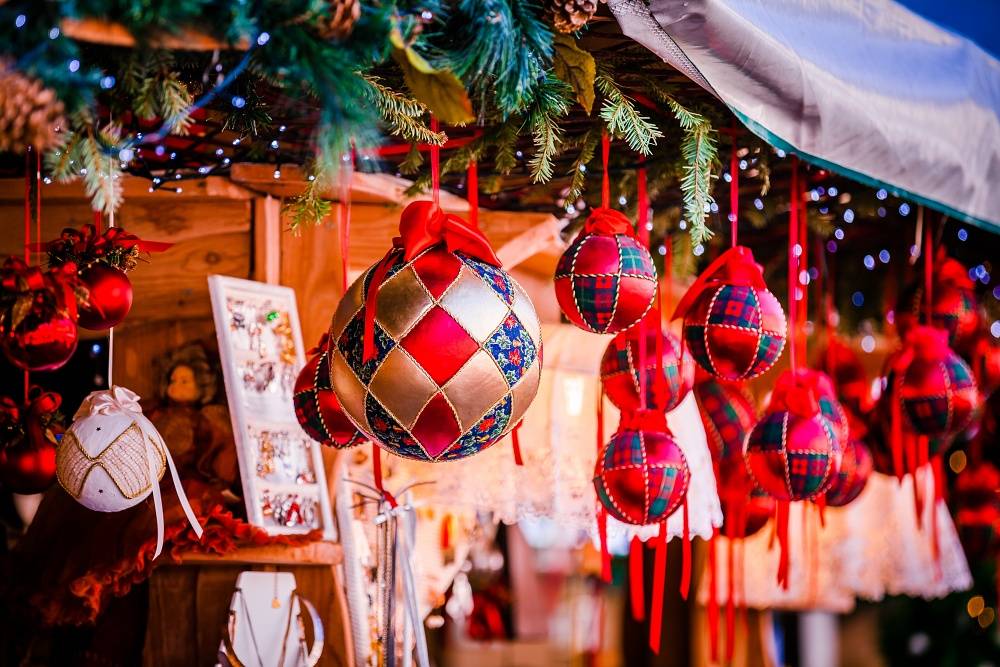 Ein Anblick einer festlich dekorierten Verkaufsbude mit Tannenzweigen, Lichtern und malersisch schönen Christbaumkugeln.