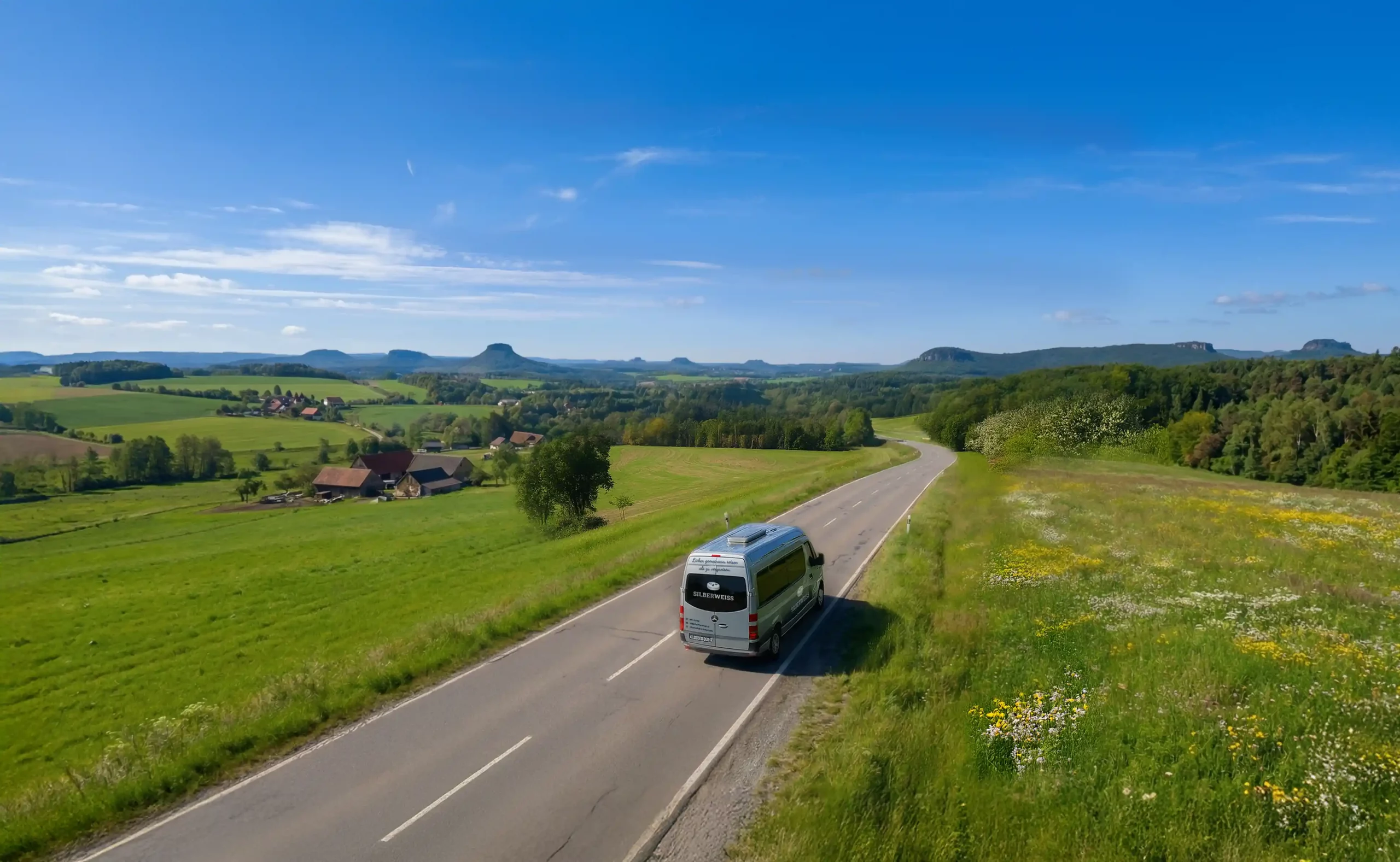 SILBERWEISS-Kleinbus fährt auf einer Landstraße durch die grüne Landschaft der Sächsischen Schweiz – Seniorenausflüge und Tagestouren rund um Dresden