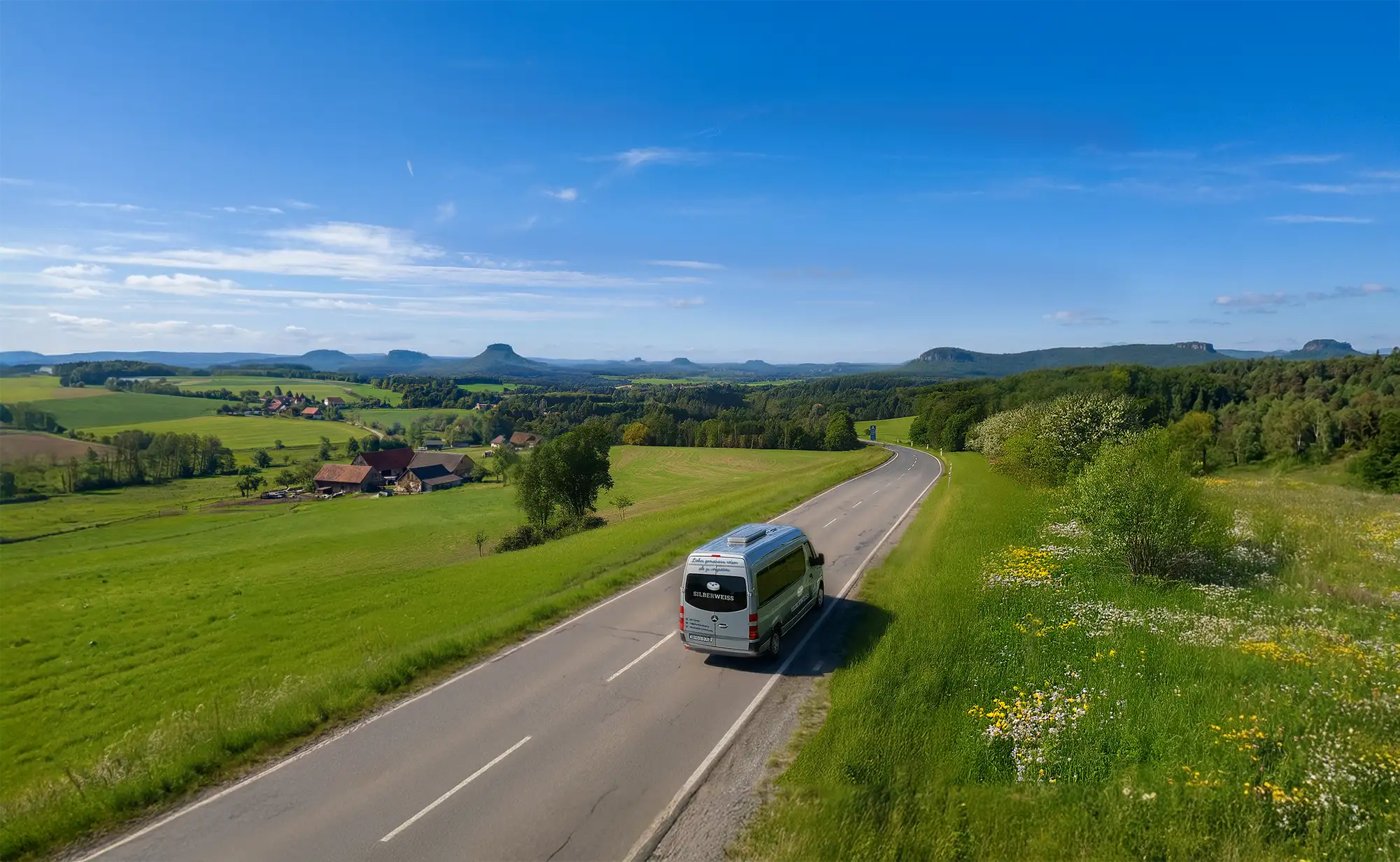 SILBERWEISS-Kleinbus fährt auf einer Landstraße durch die grüne Landschaft der Sächsischen Schweiz – Seniorenausflüge und Tagestouren rund um Dresden